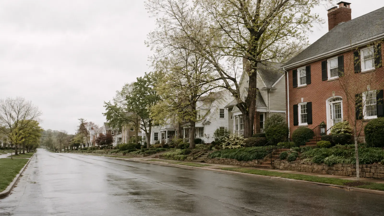 A residential street of older brick and sided homes on an overcast day