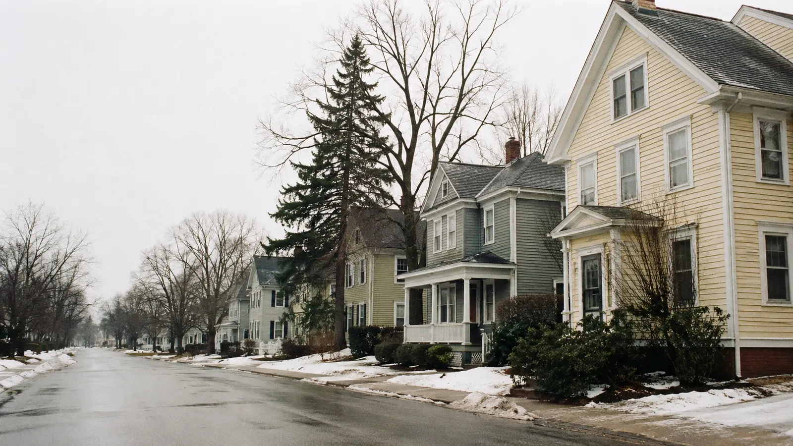 A residential street of older wood-sided homes on a gray, damp day